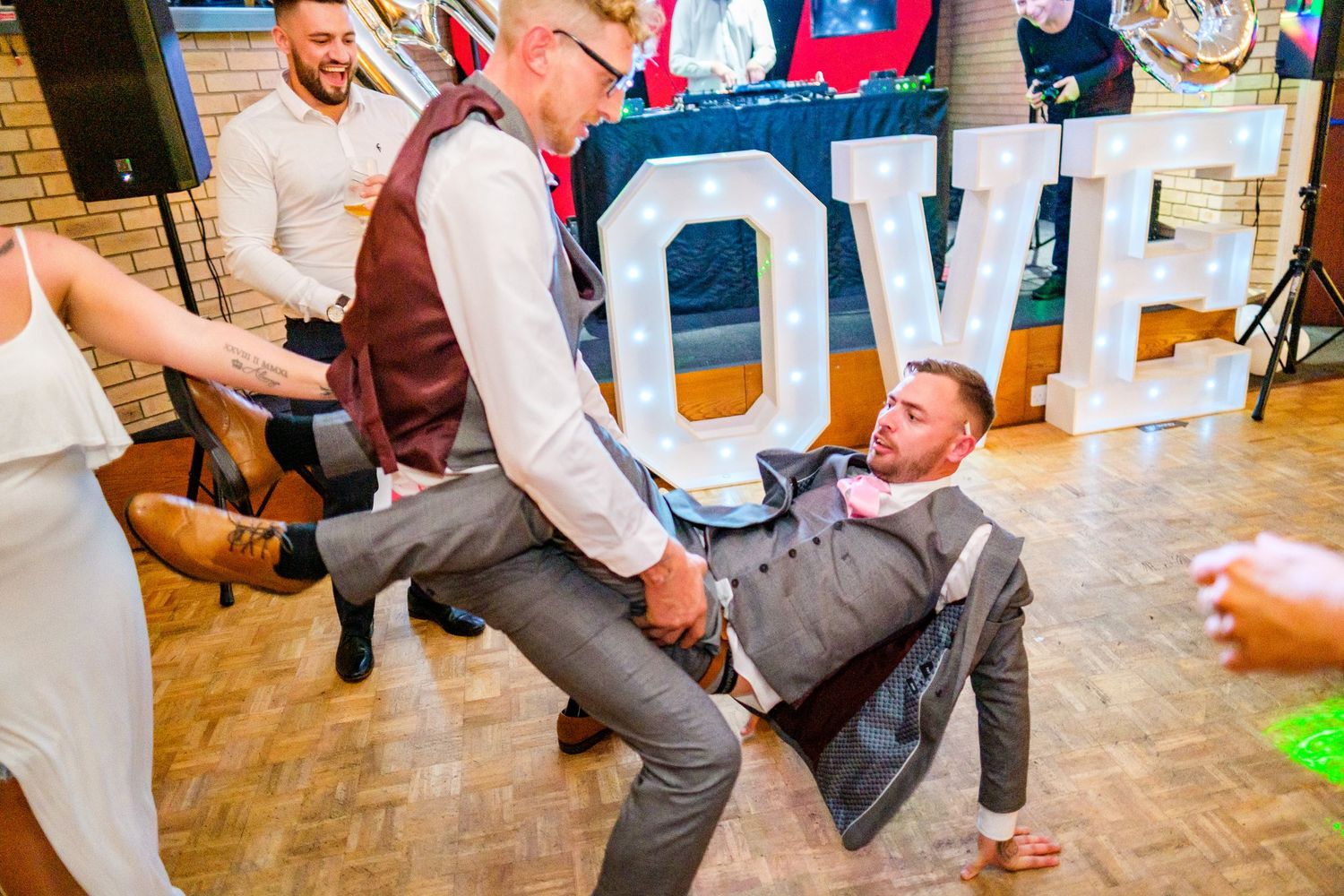 Wedding guests perform energetic dance moves during reception celebration.