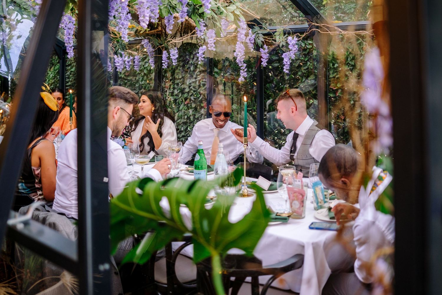 Wedding reception setup with purple wisteria decorations hanging from above and elegant table settings.