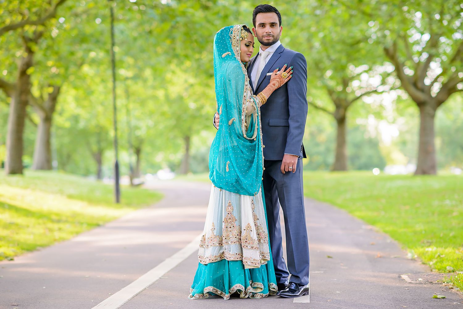 Wedding couple poses along tree-lined path in park with turquoise and navy attire.