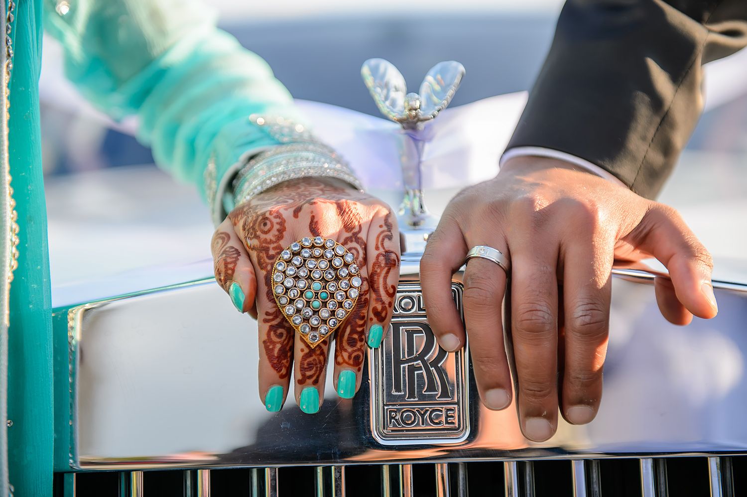 Close-up of hands with traditional henna design next to a Rolls Royce emblem.