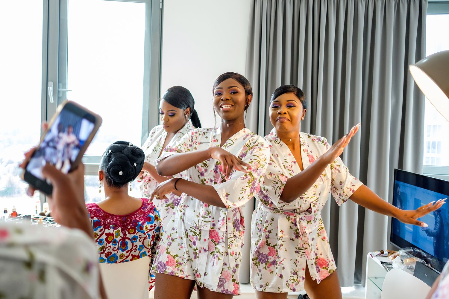 Bridesmaids in floral robes laughing and celebrating during pre-wedding preparations.