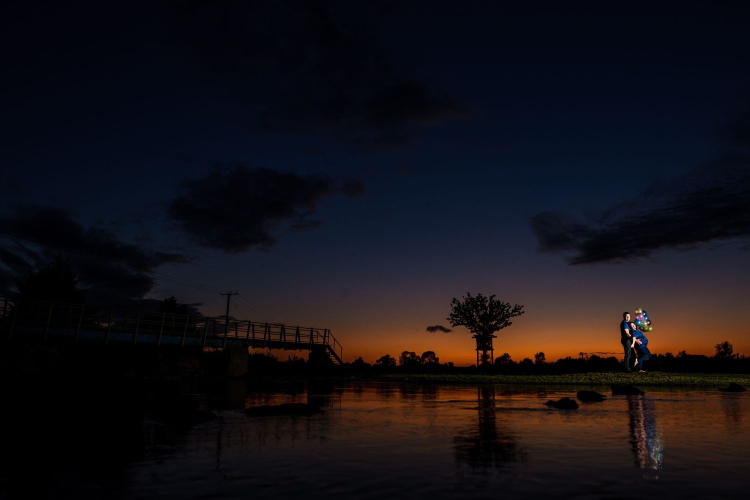 Dark silhouettes of trees against a dramatic orange and purple sunset sky over tranquil water.