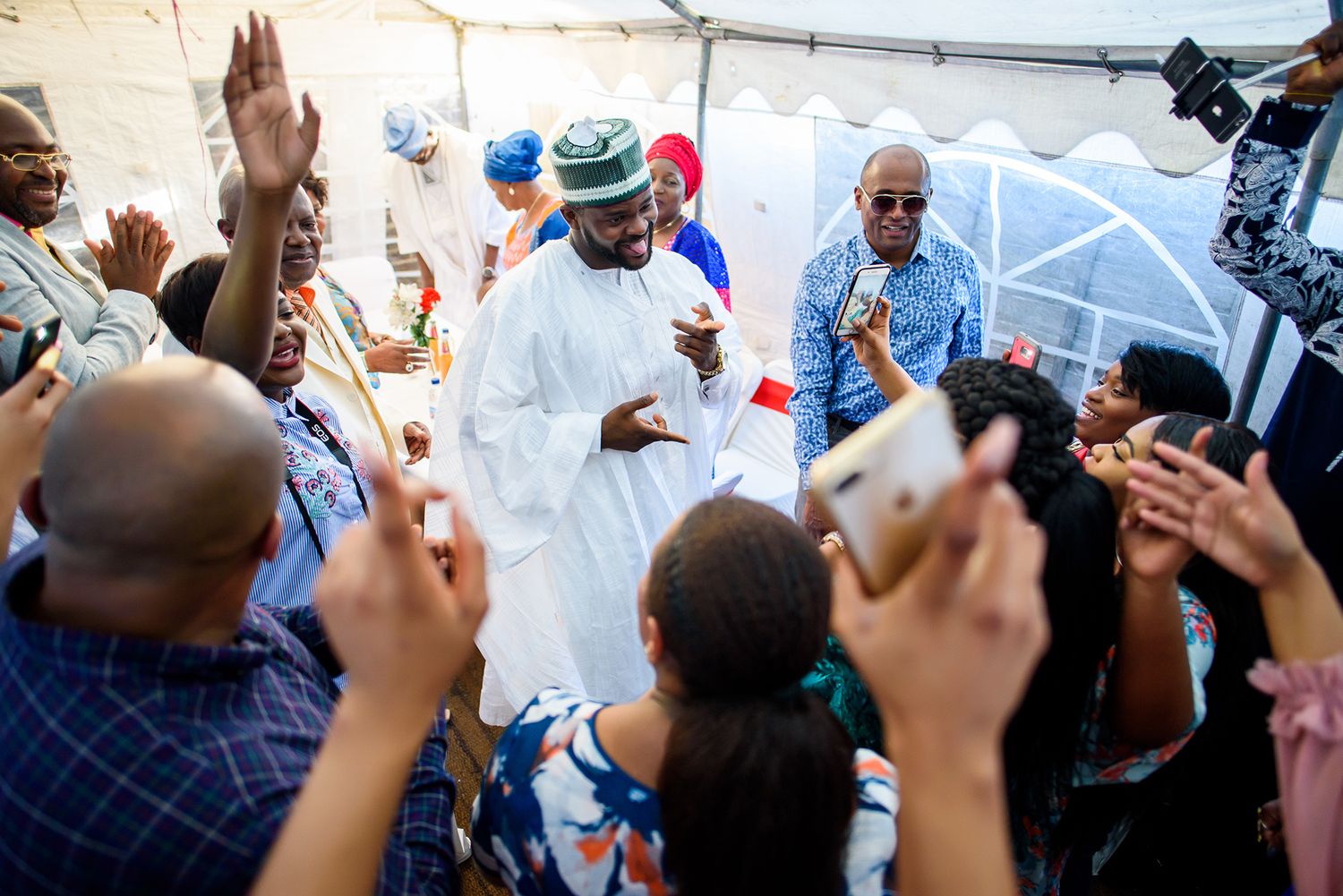 Festive crowd with raised arms dancing and celebrating under white tent.