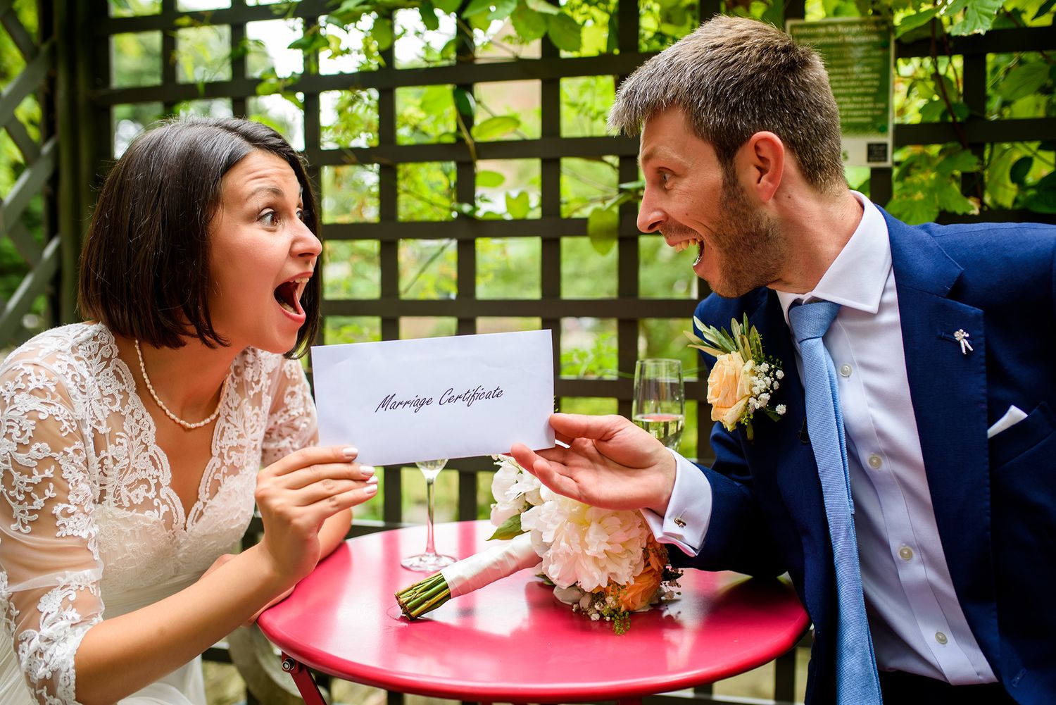Couple shares playful moment at outdoor garden table during wedding.