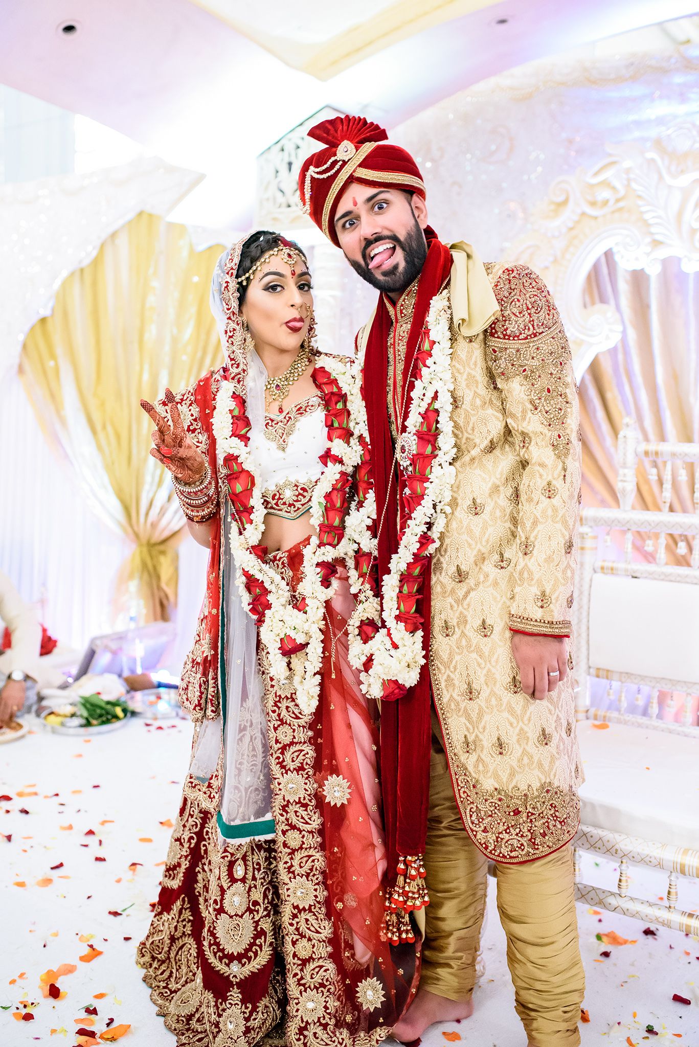 Traditional Indian wedding ceremony with couple in ornate red and gold attire standing at decorated mandap.