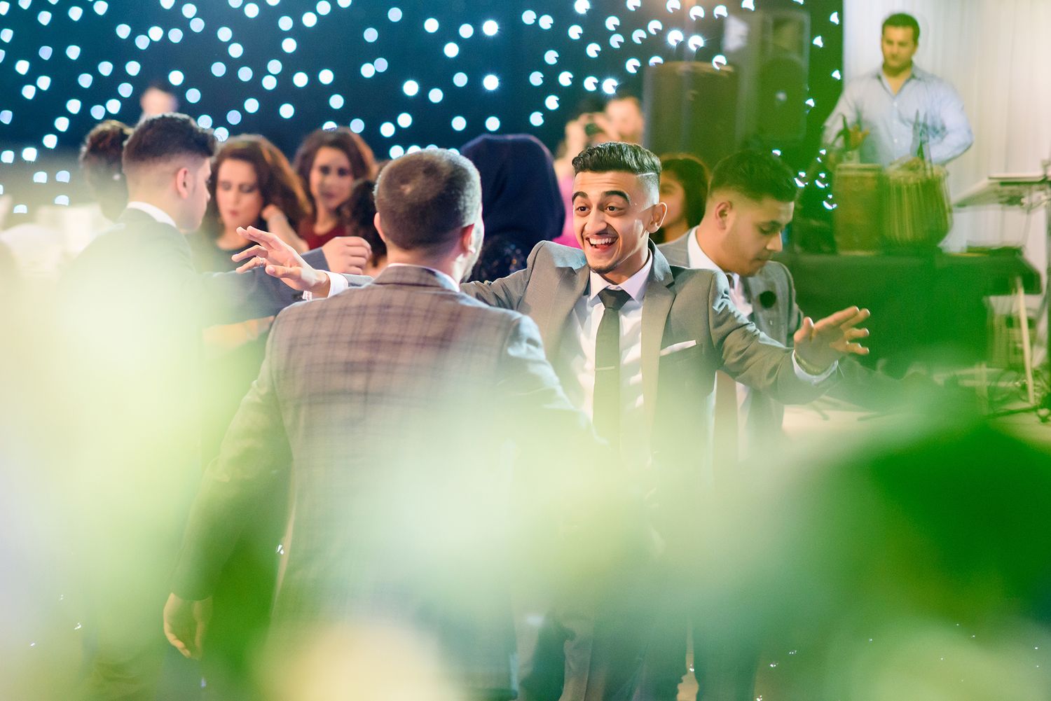 Wedding celebration scene with bokeh lights and greenery in foreground.