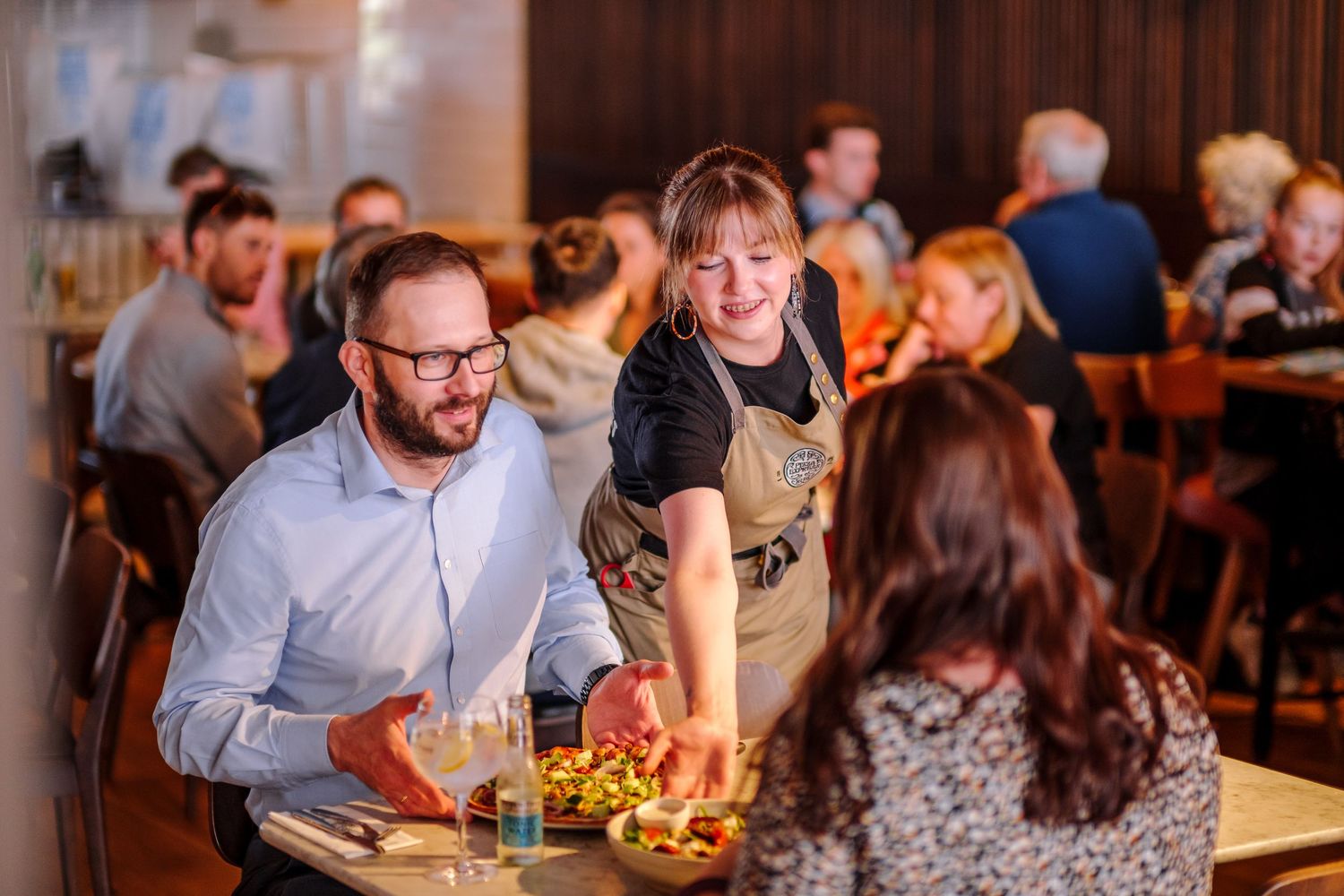 Restaurant dining room filled with guests enjoying dinner at tables with warm ambient lighting.