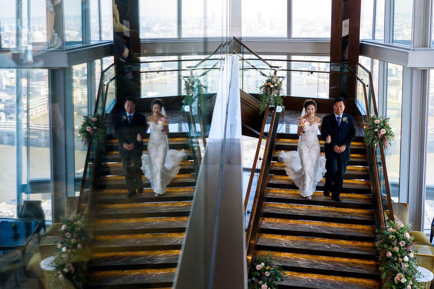 Two parallel staircases decorated with greenery and white fabric in an elegant indoor venue with large windows.