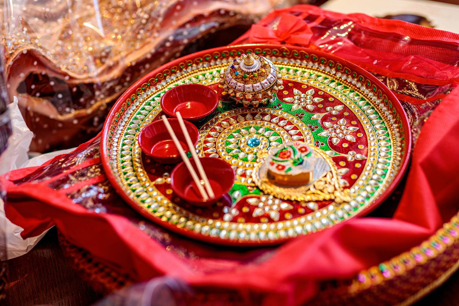 Traditional Indian thali plates decorated with intricate red and gold designs displayed on red fabric.