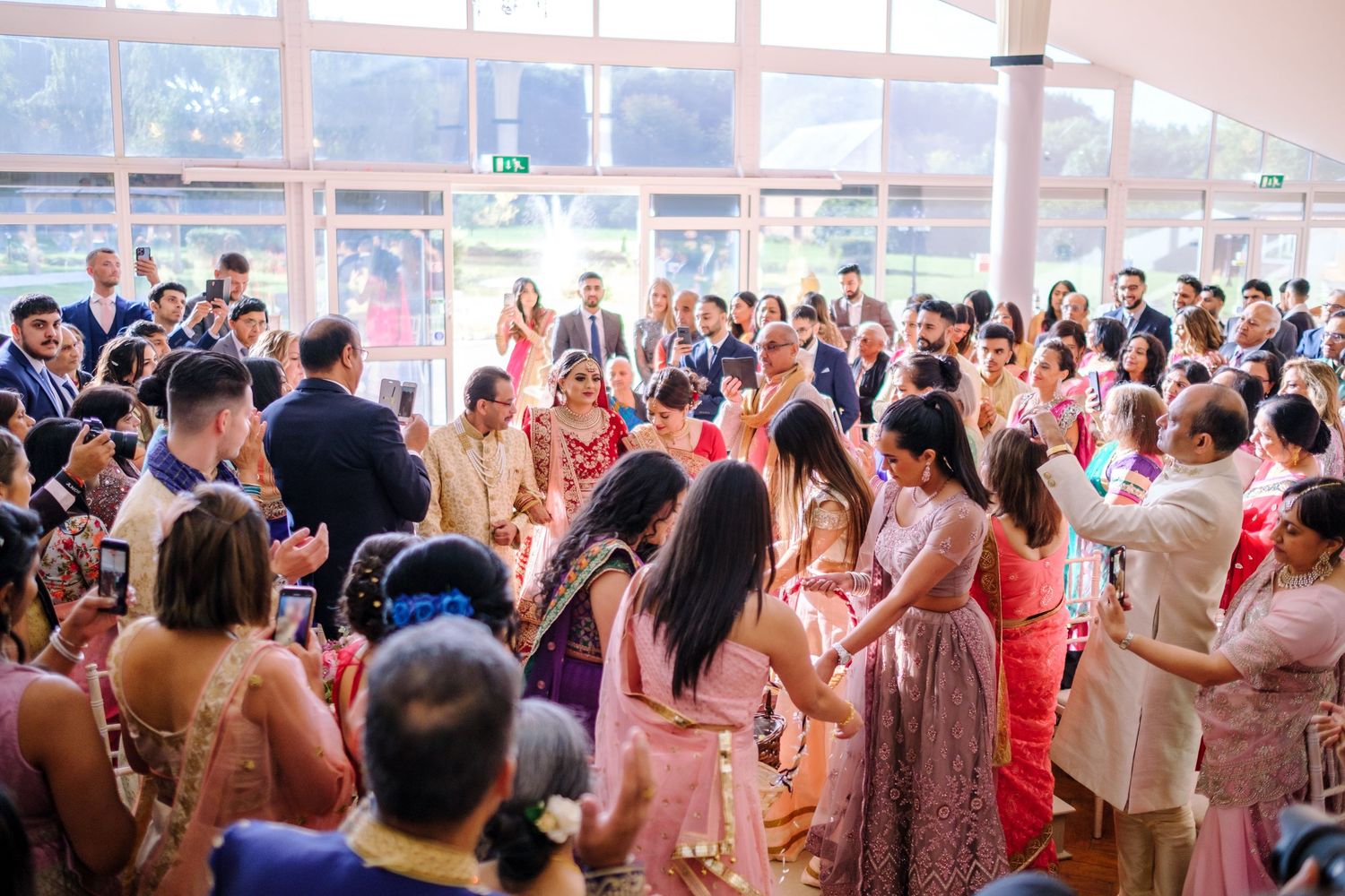 Large crowd of wedding guests in colorful attire celebrating during an Indian wedding reception.