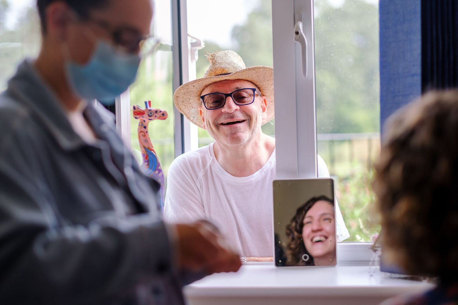 People having a video call meeting with one person on a tablet screen while others sit around a table.