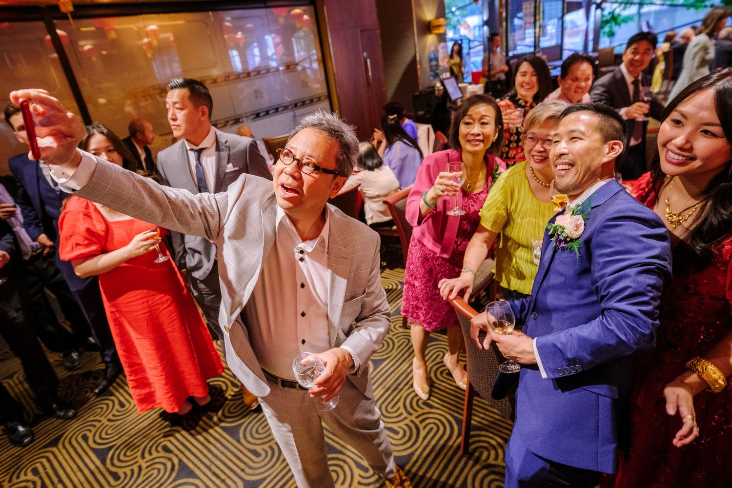 Wedding guests dance and celebrate together on a patterned carpet dance floor at an indoor reception venue.