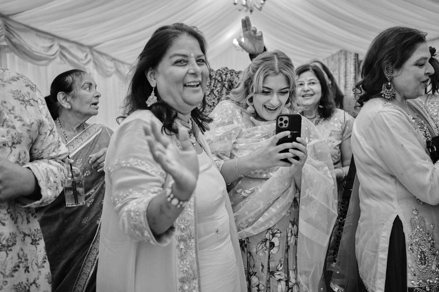 Black and white photo of wedding guests dancing and celebrating together at a reception party.