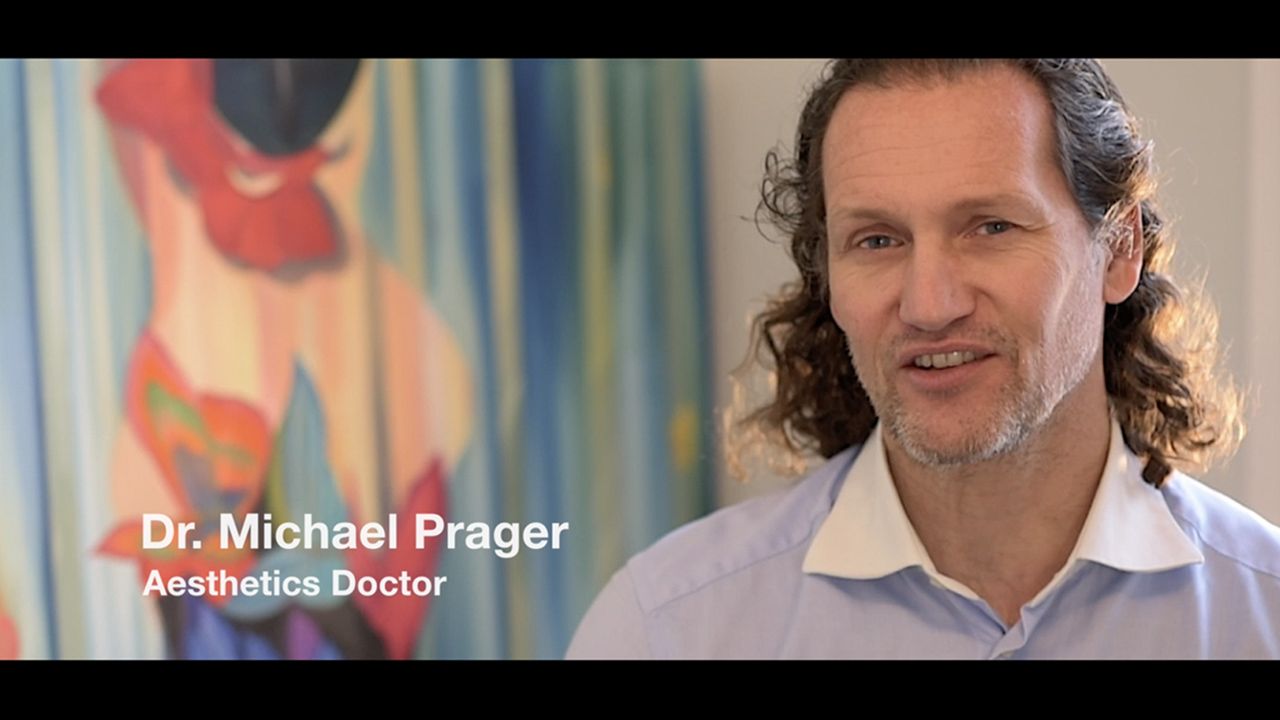 Dr. Michael Prager, Aesthetics Doctor, speaking on camera in a professional setting with colorful artwork in the background.