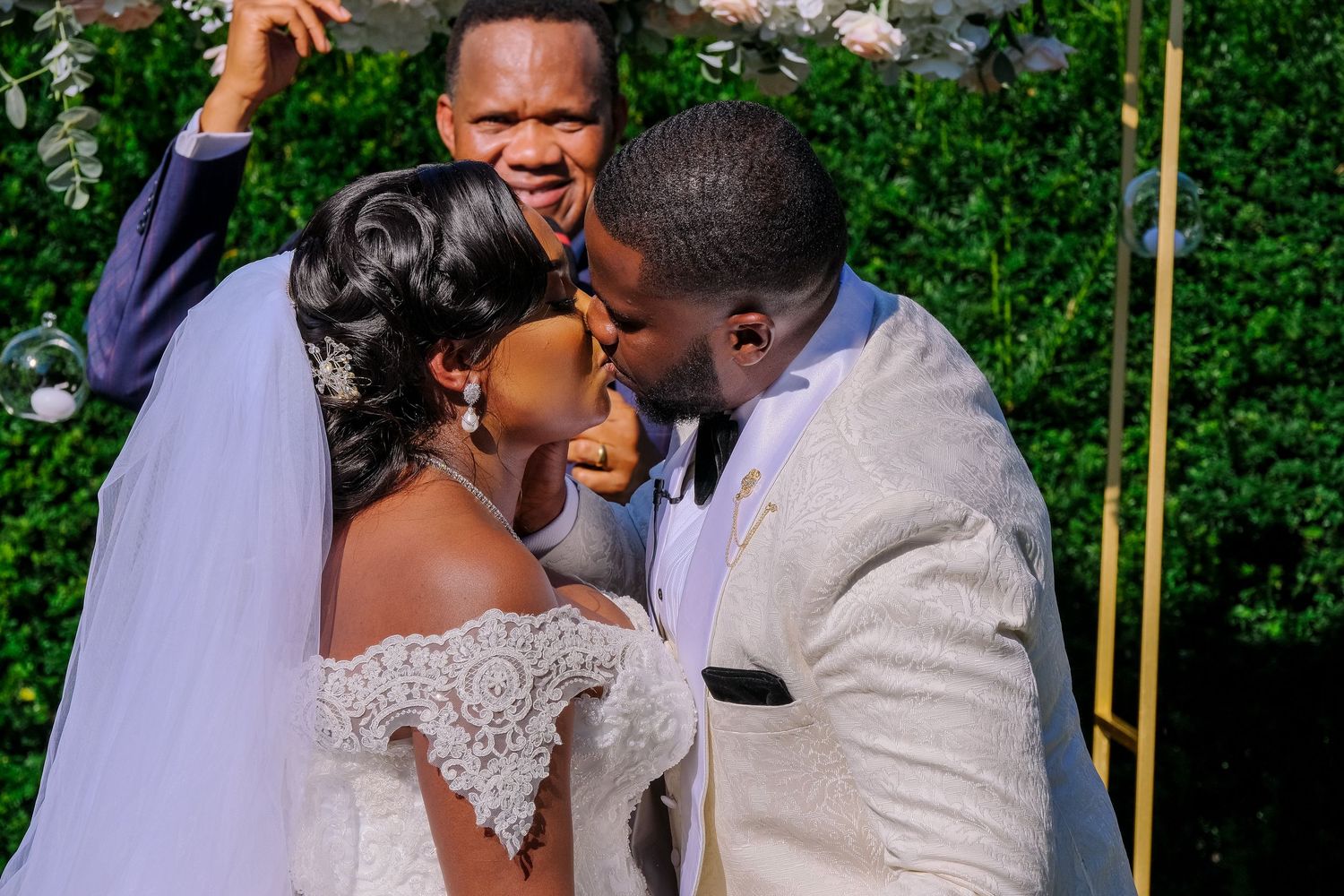 Couple shares a romantic moment during outdoor wedding ceremony surrounded by lush greenery.
