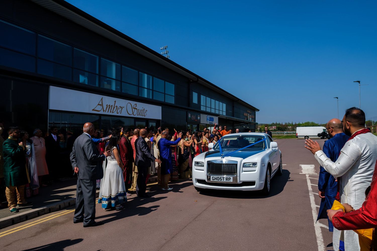 A line of luxury cars parked outside a modern building under bright blue skies.