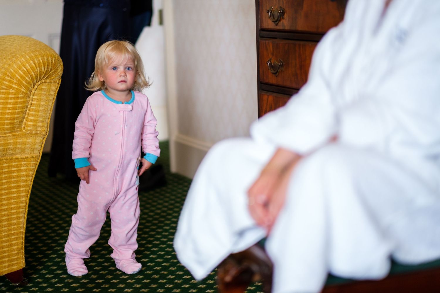 A small child in pink pajamas plays with adults in a warmly lit room.