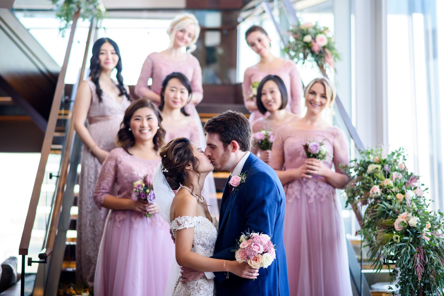 Wedding party in pink bridesmaid dresses celebrating in an elegant venue with floral decorations.