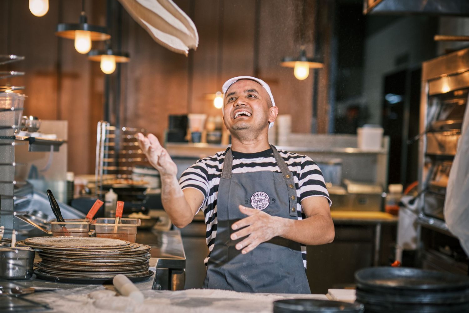 Restaurant worker tossing pizza dough in the air at a pizzeria kitchen.