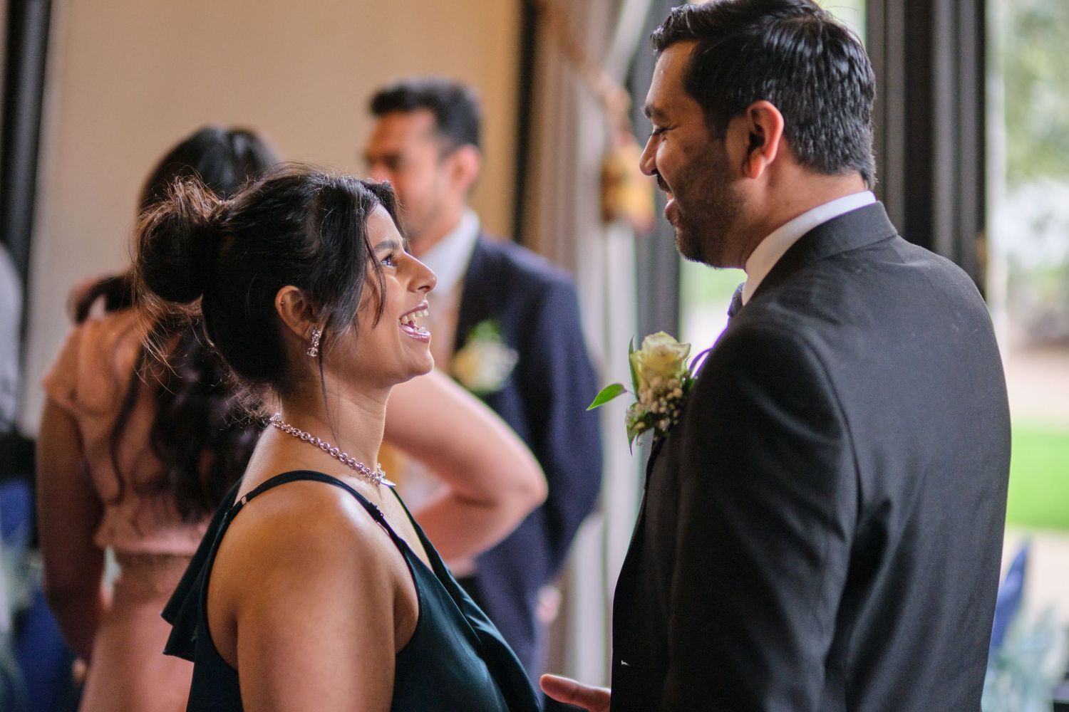 A couple shares a tender moment during their wedding reception as guests mingle in the background.