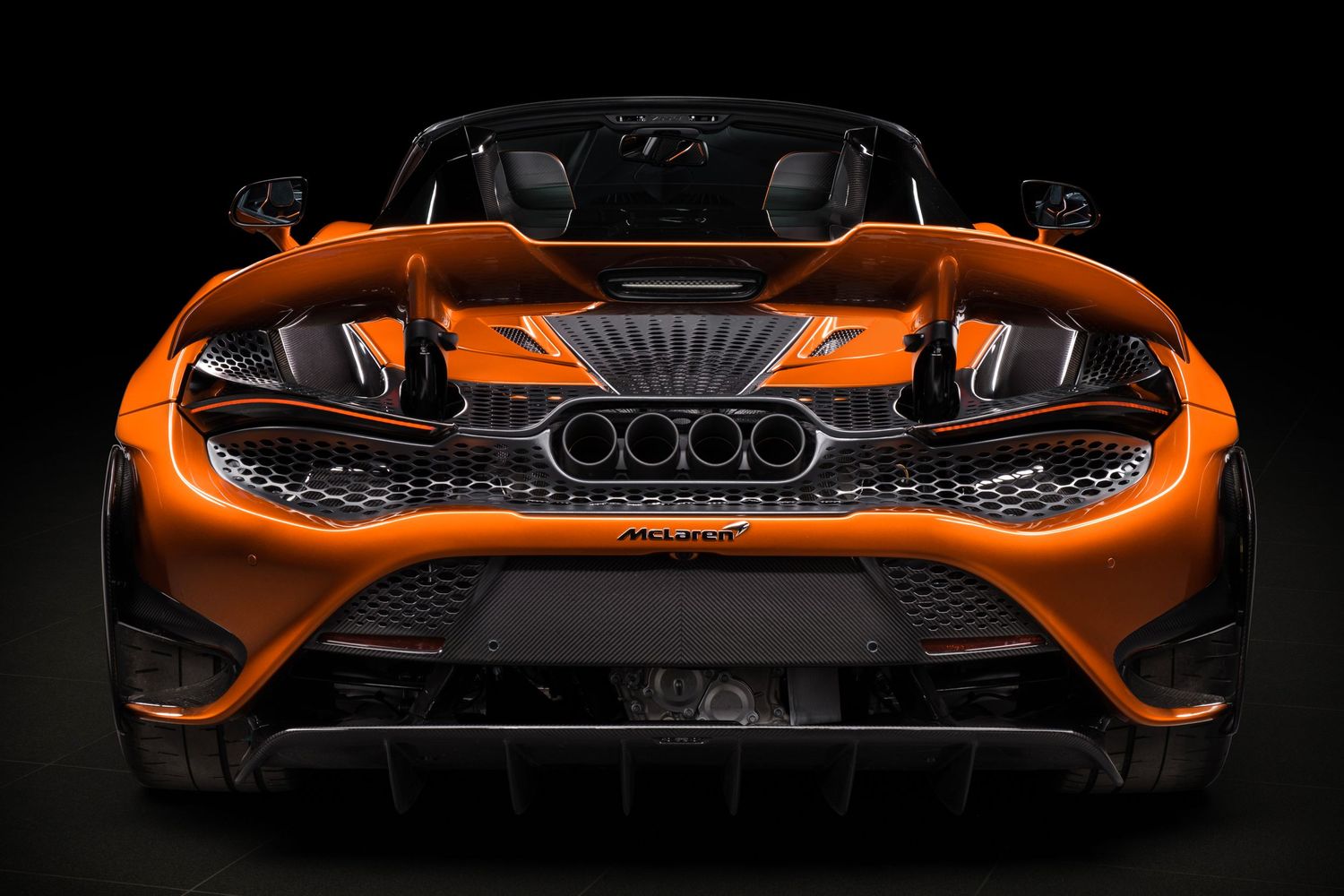 Close-up view of an orange McLaren supercar's aggressive front end design against a black background.
