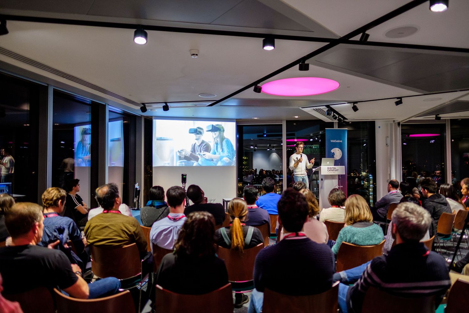 Audience watching presentation in modern office space with dynamic lighting.