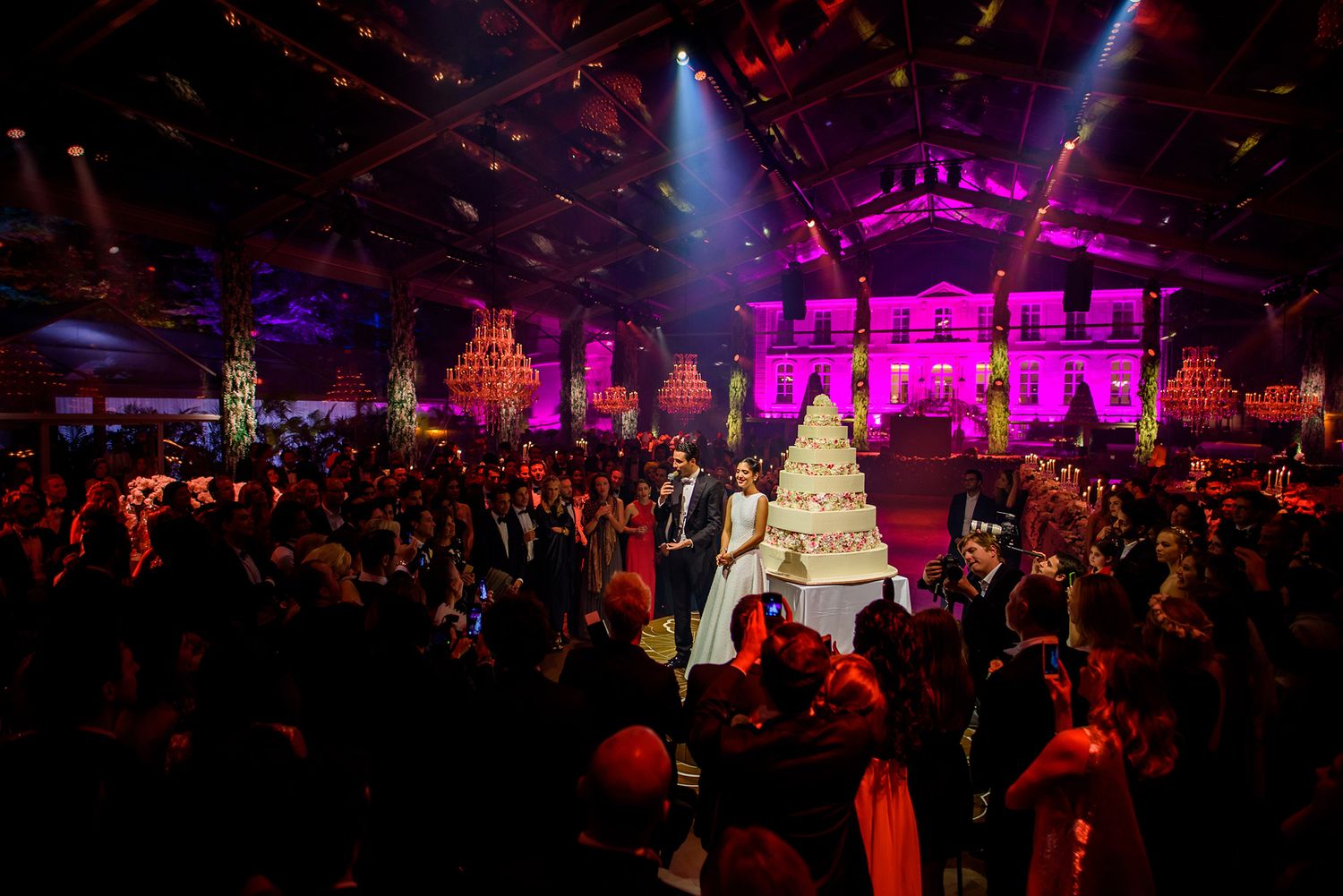 Concert-style lighting in purple and red illuminates a packed event space during a celebration.