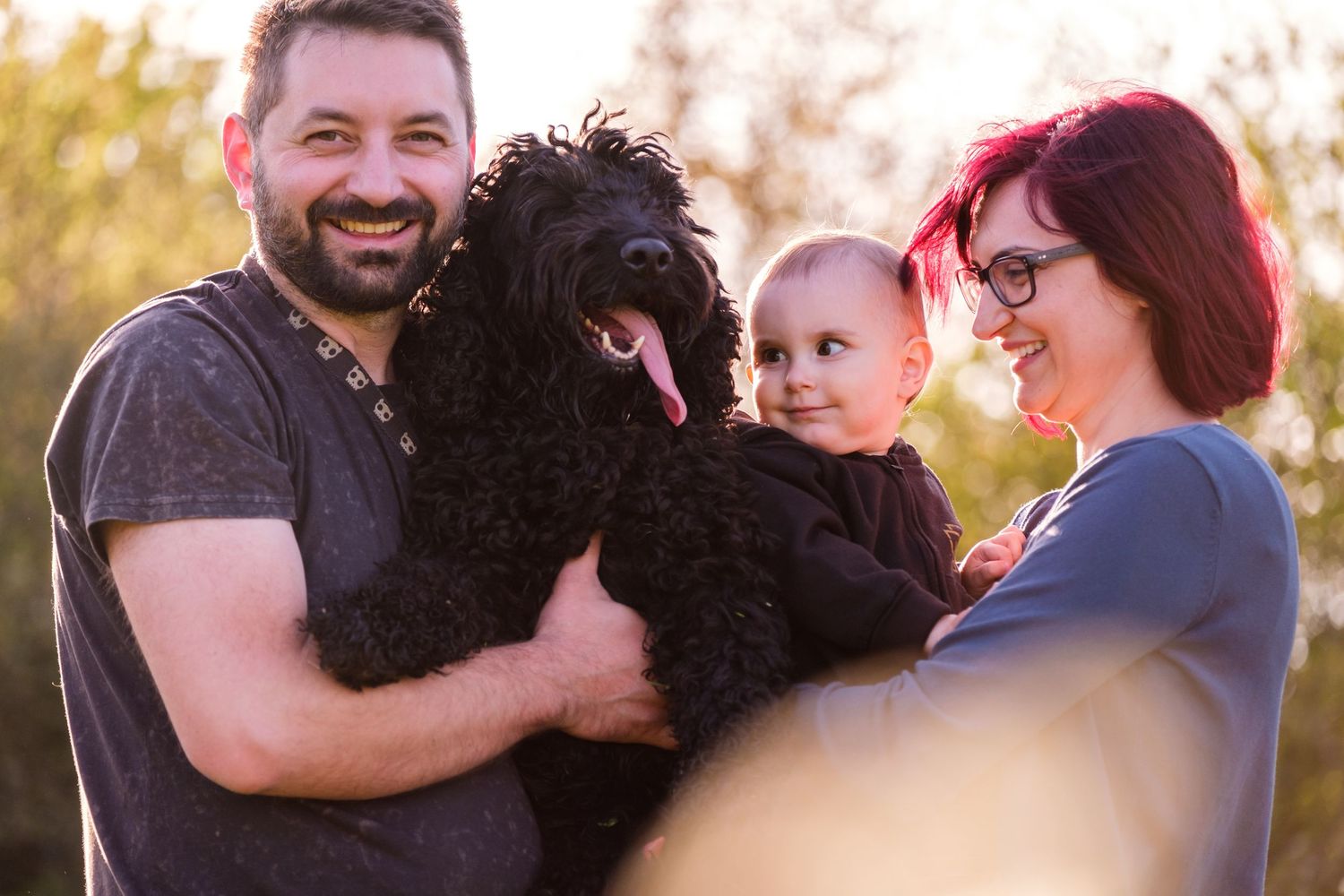Family members hugging and sharing joyful moments during golden hour portrait session in natural setting.