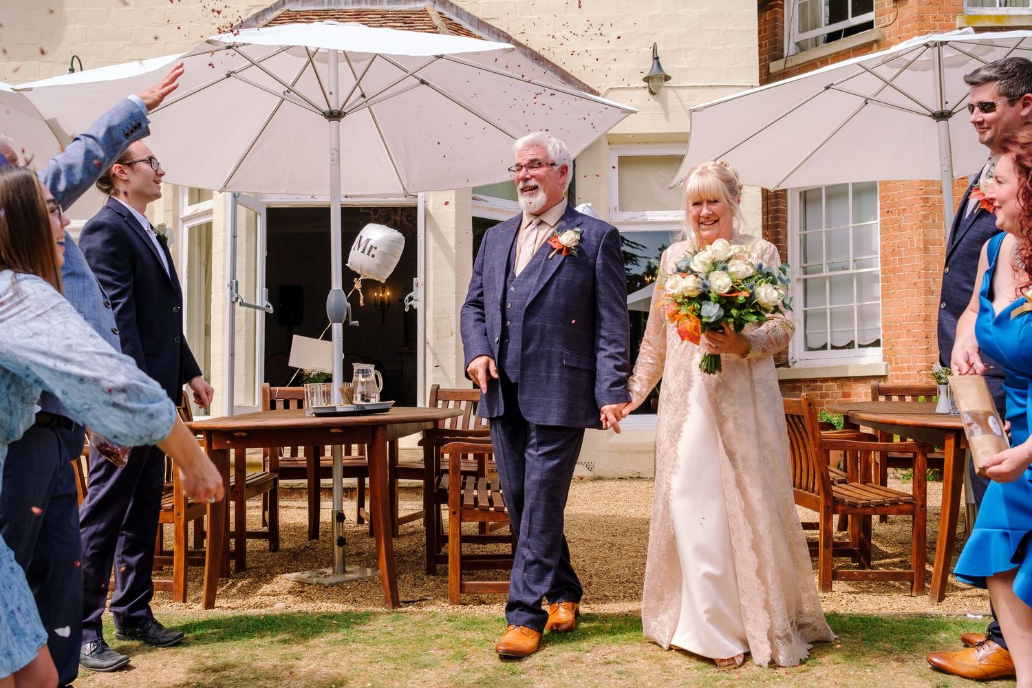 Wedding guests gather on a wooden deck outside a venue during an outdoor celebration.
