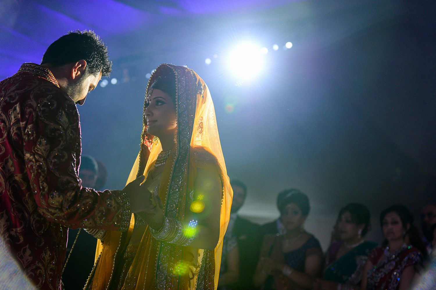 Traditional Indian wedding ceremony with couple in ornate attire under dramatic stage lighting.