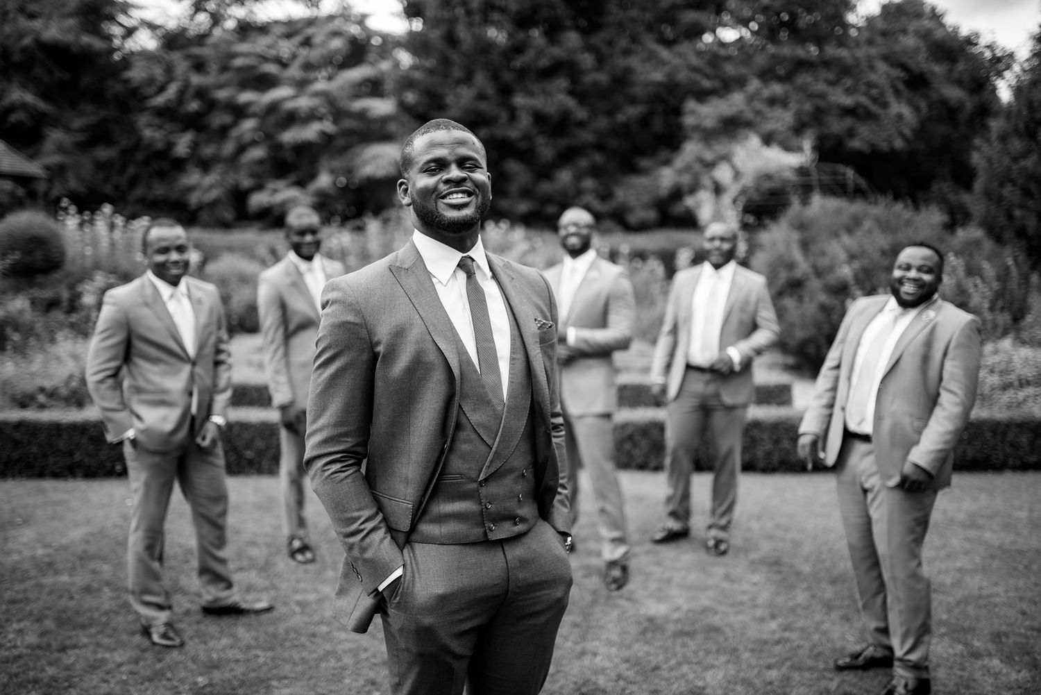 Groomsmen in gray suits share laughs and smiles during an outdoor wedding photoshoot.