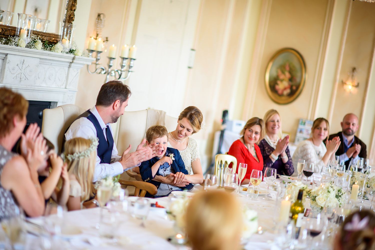 Wedding guests laughing and socializing at elegant reception dinner with wine glasses and place settings.