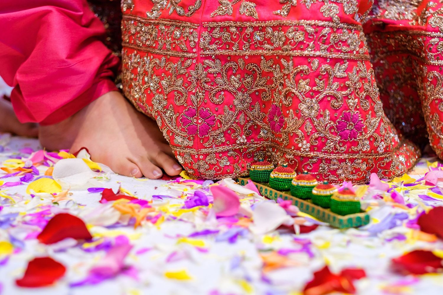 Detail shot of pink and gold embroidered fabric with rose petals scattered on floor.