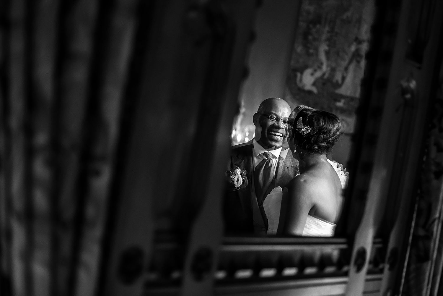 Black and white wedding photograph captured through a decorative frame showing joyful moments.