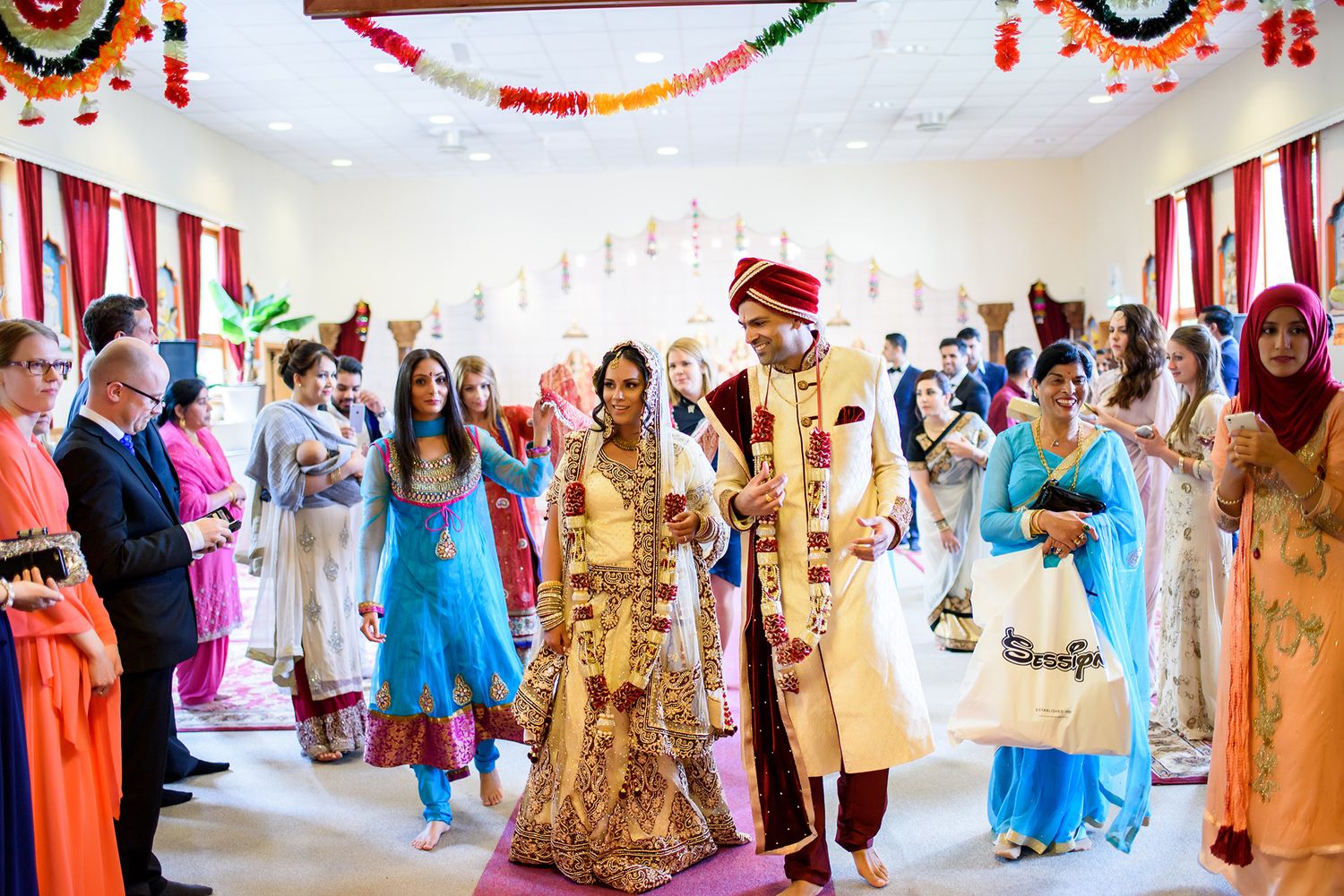 Panoramic view of decorated Indian wedding venue with guests in colorful traditional outfits.