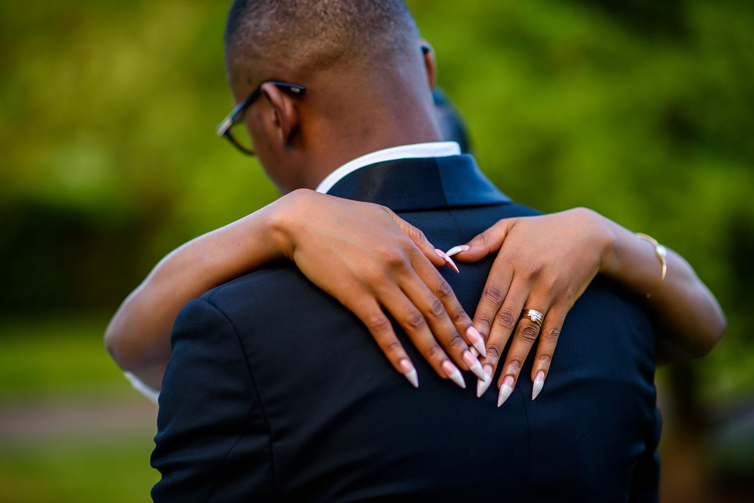 Close-up detail of hands resting on black tuxedo jacket at wedding.