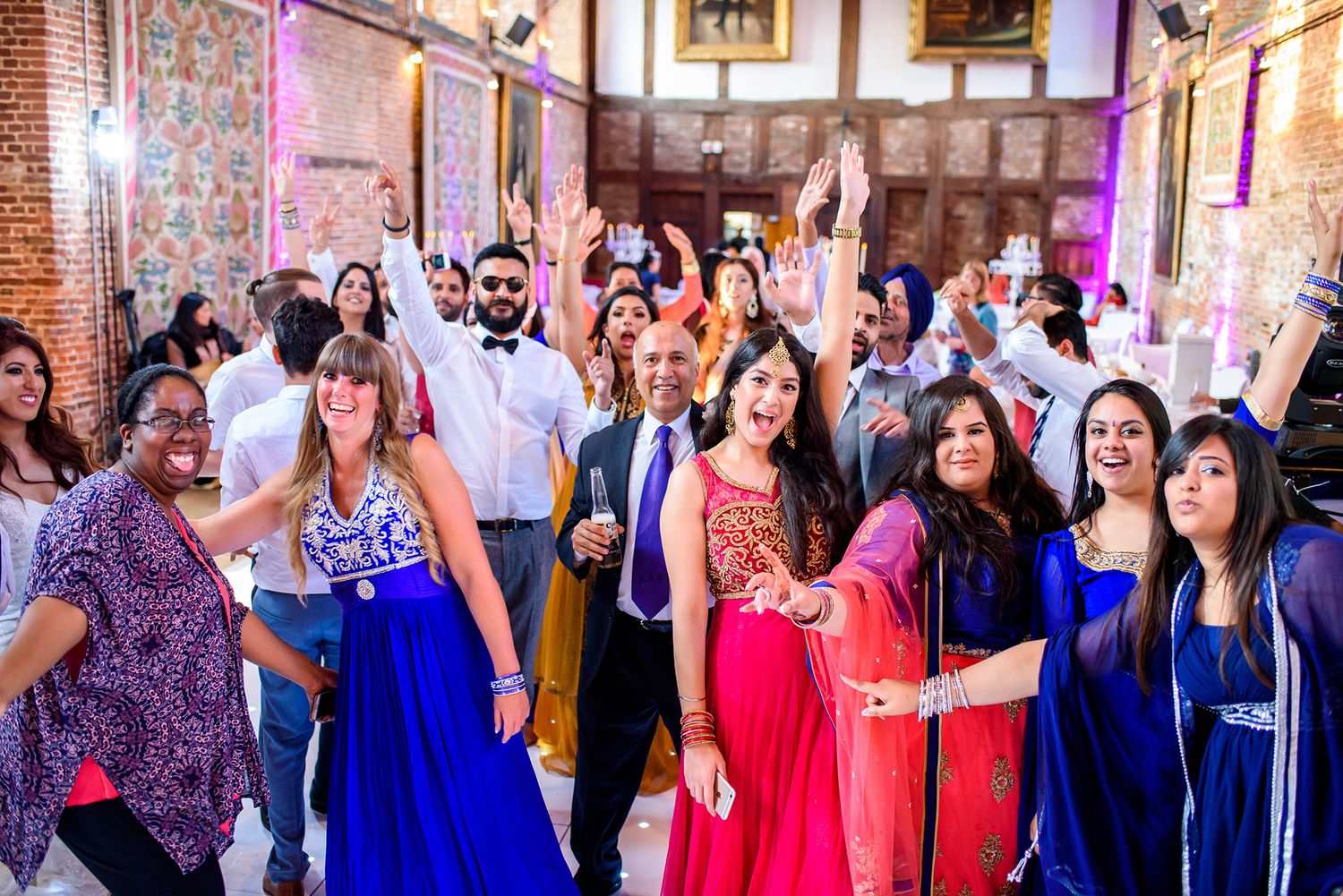 Wedding party guests in vibrant blue and red formal attire pose together.