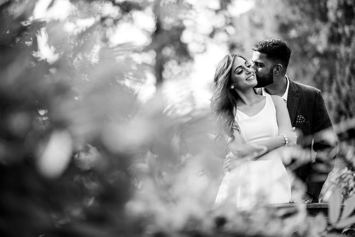 Black and white romantic moment captured through soft bokeh in an outdoor setting.