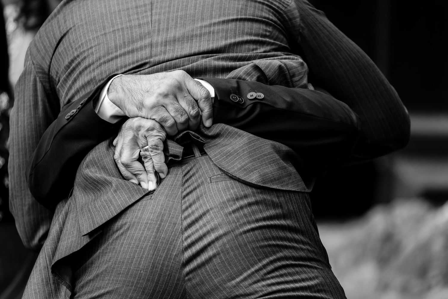 Black and white close-up of hands and formal suit jacket.