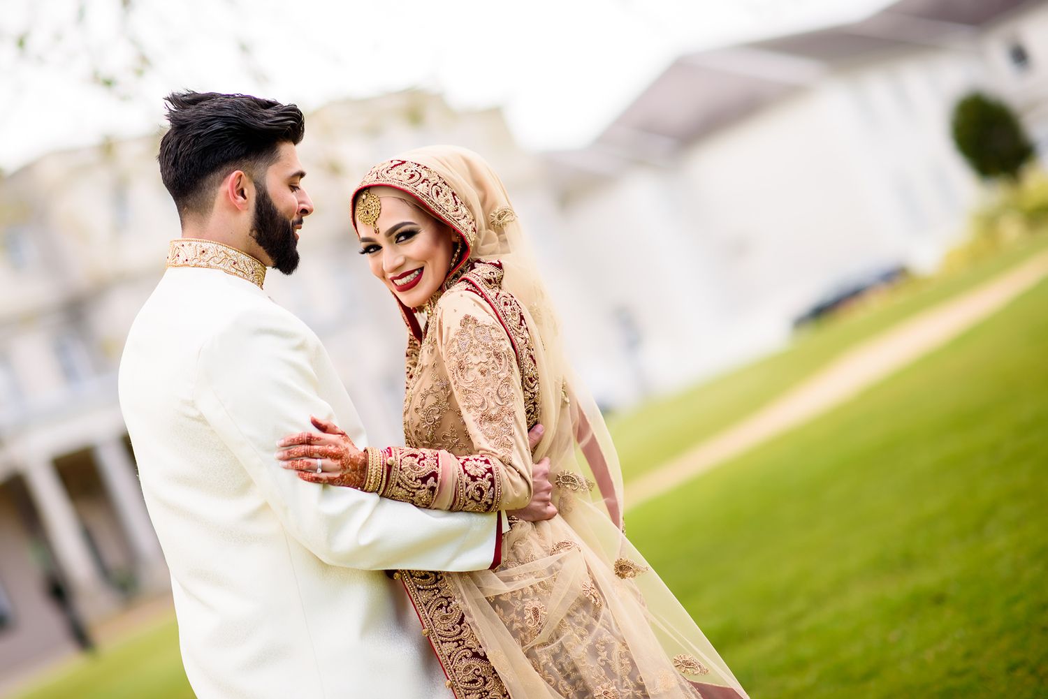 A couple in elegant wedding attire dance together on a manicured lawn.