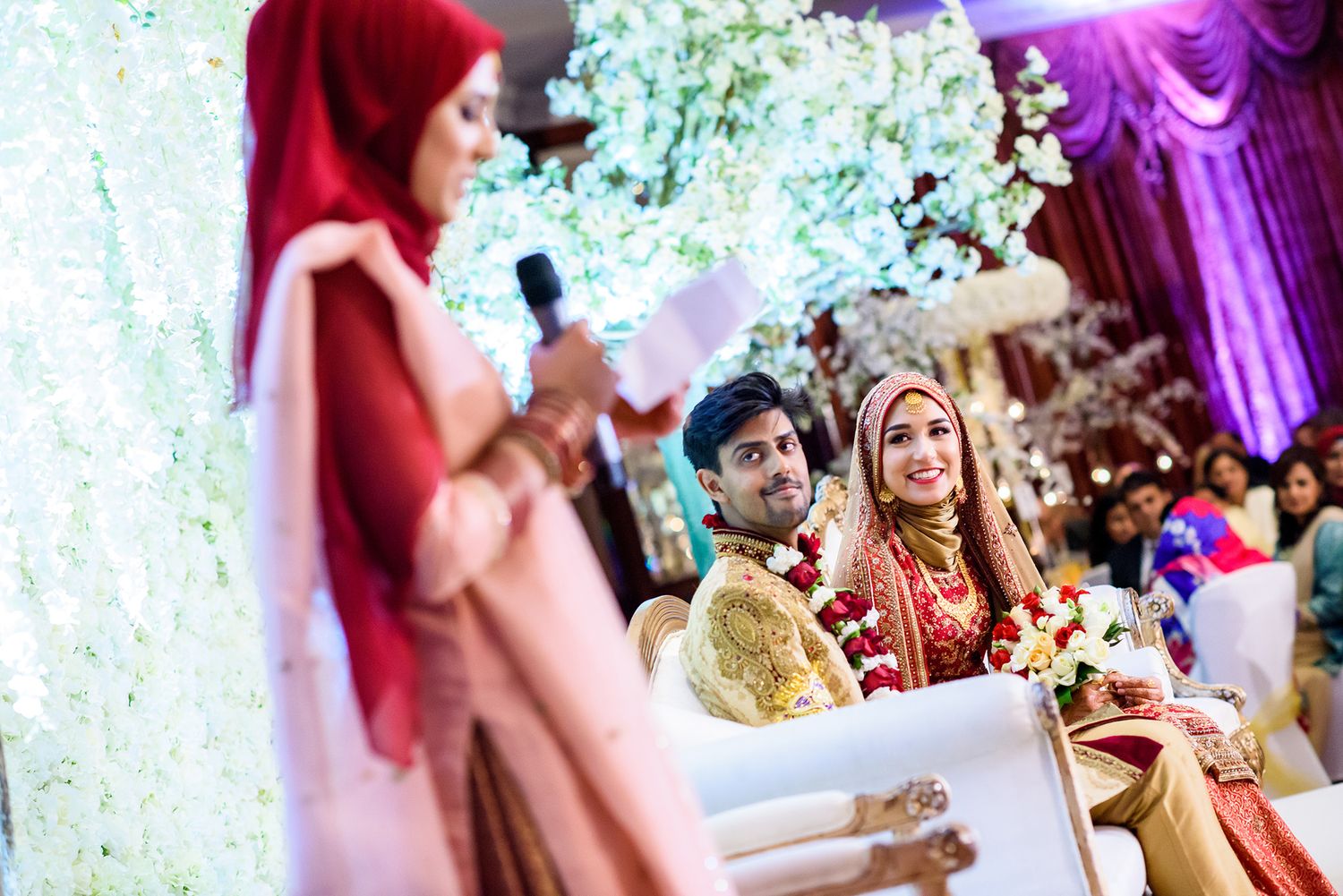 Wedding reception venue decorated with purple lighting and white floral arrangements.