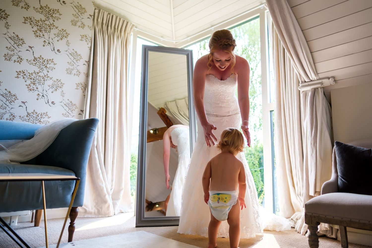Elegant bridal preparations in a sunlit room with floral wallpaper and white decor.