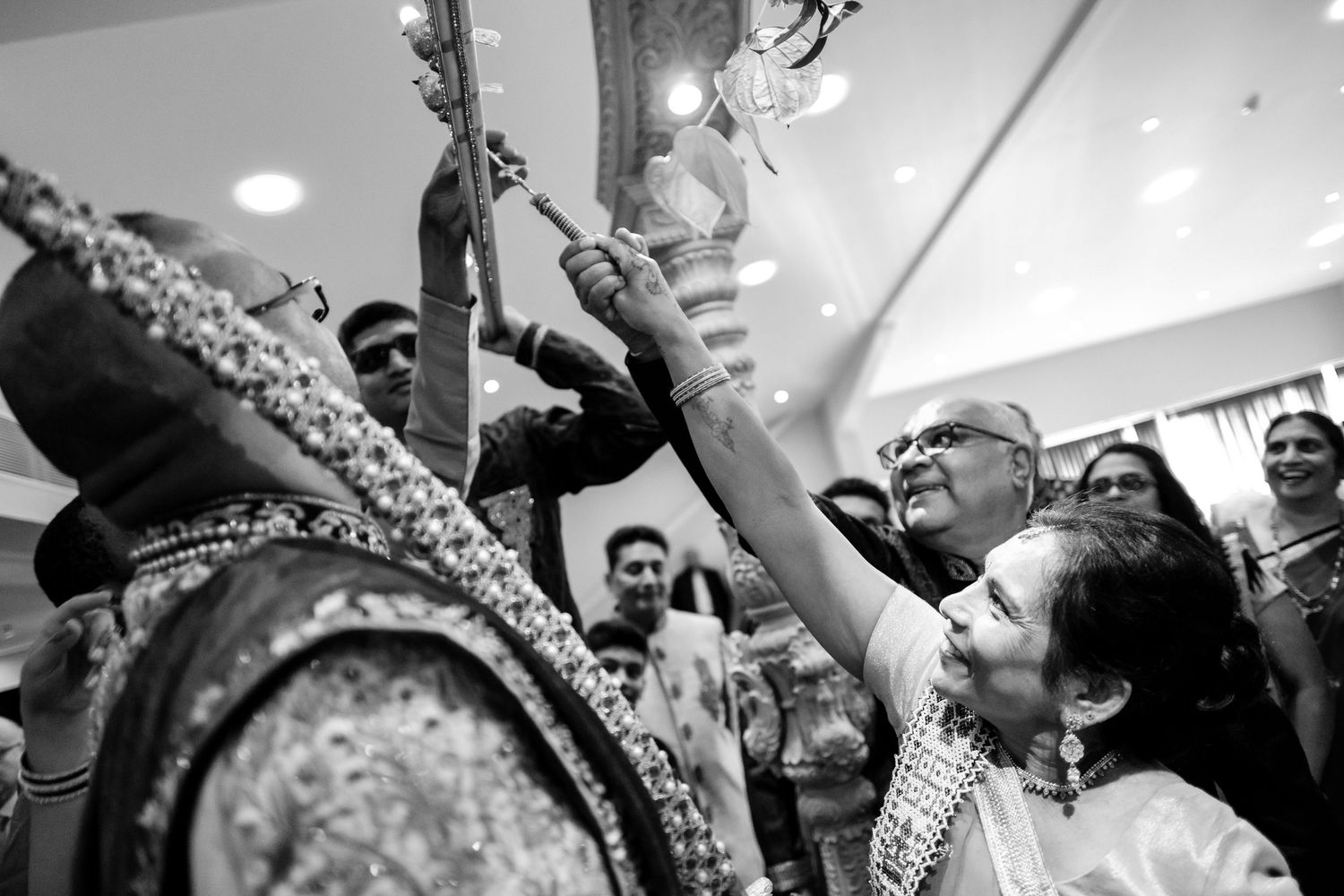 People gather around and reach up to touch an ornate religious statue or shrine in black and white photography.
