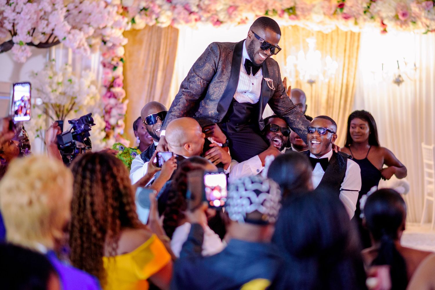 Wedding guests celebrate as someone is lifted up during a lively reception dance party.