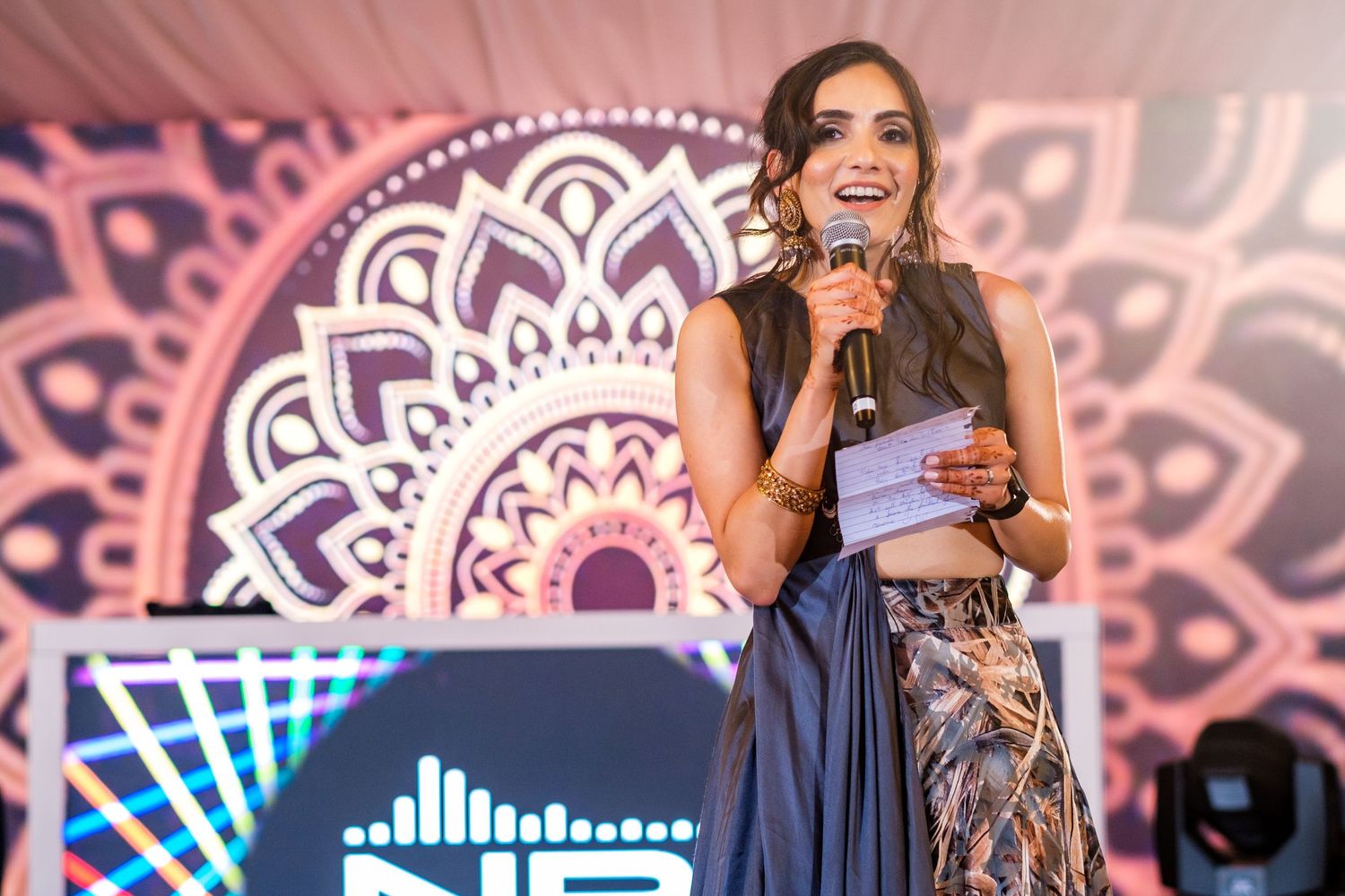 Evening wedding reception speech with decorative mandala backdrop illuminated in pink and blue.