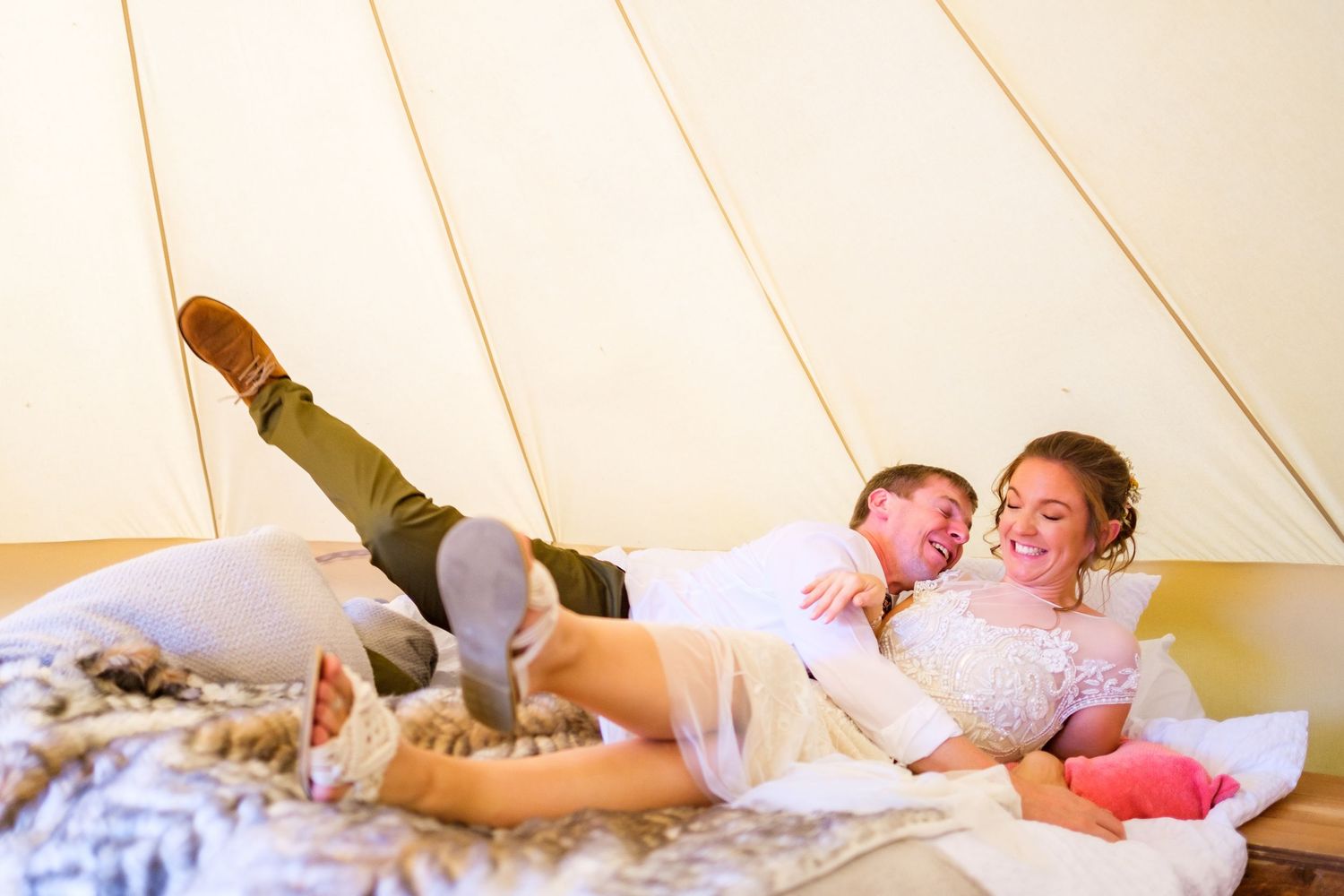 Two people sharing a playful moment while relaxing on pillows inside a tent structure.