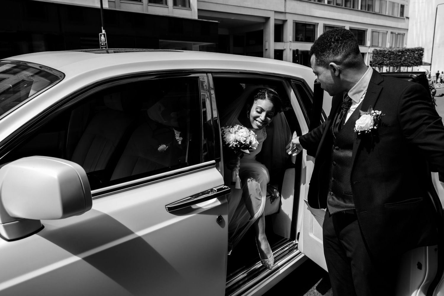 Black and white photo of luxury cars lined up outside an event venue.