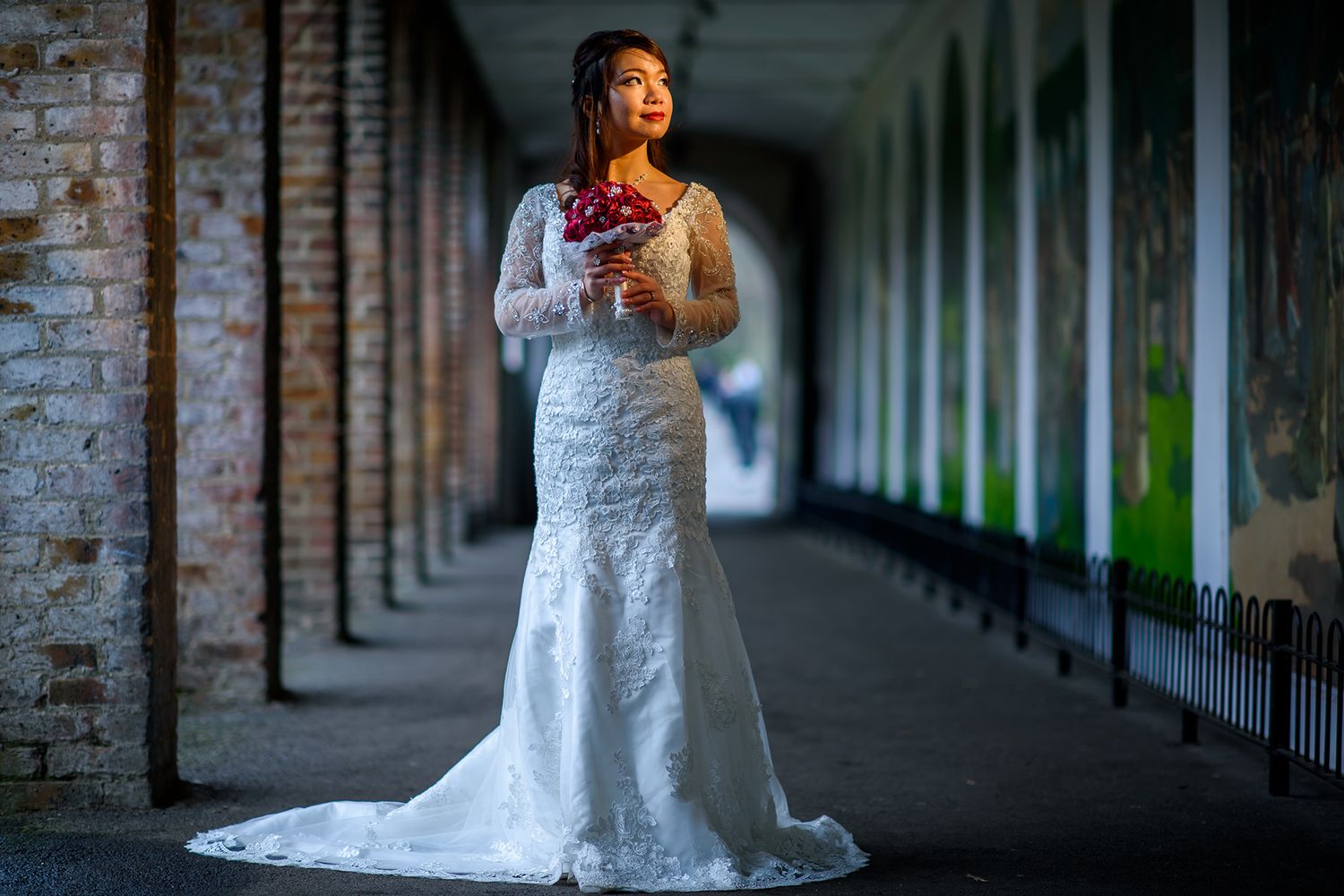 A moody wedding portrait in a dimly lit historic arcade with brick columns.