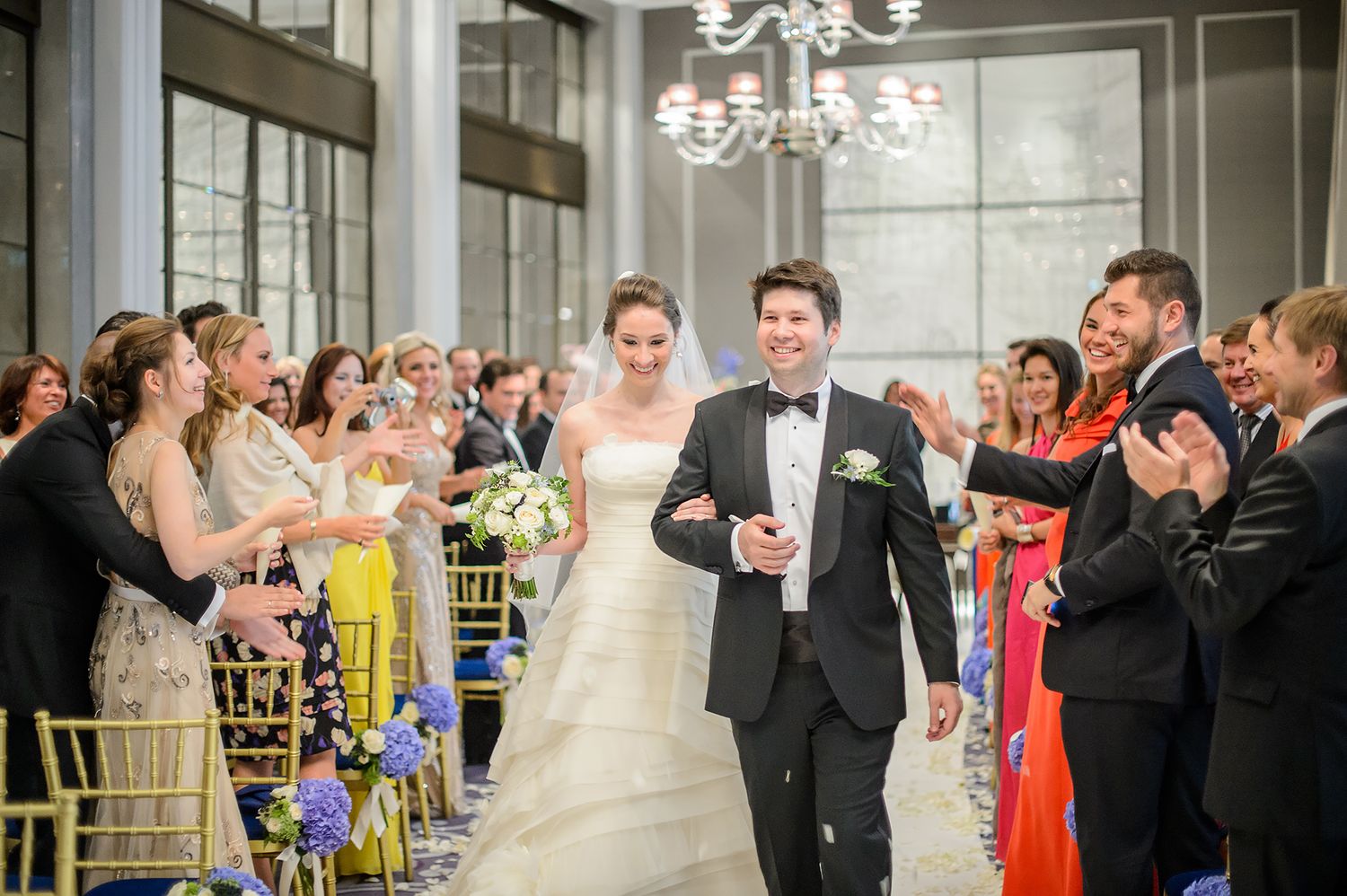 Wedding celebration in elegant hall with guests applauding along ceremony aisle.