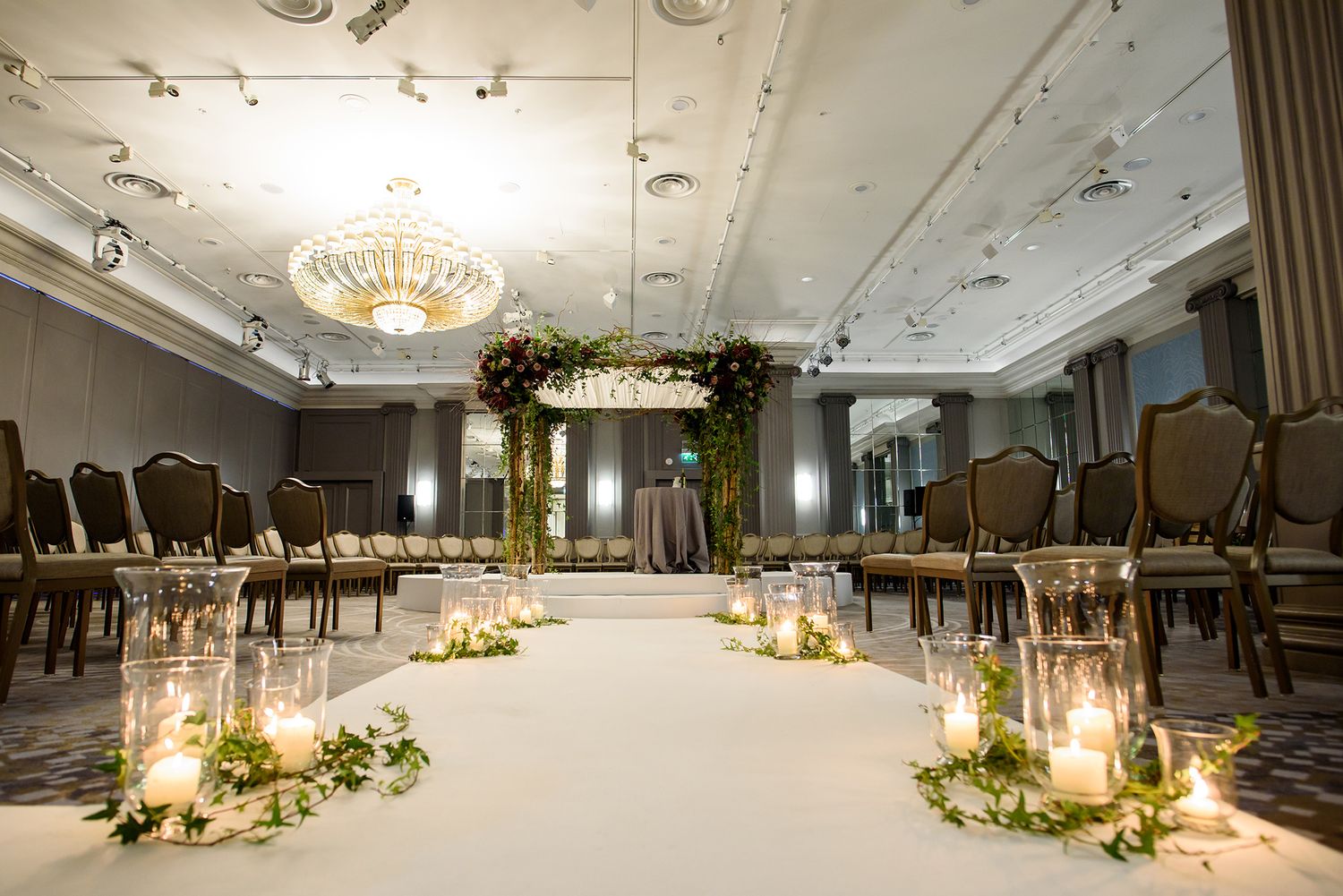 Elegant wedding venue with lantern-lit aisle and floral arrangements lining the ceremony space.